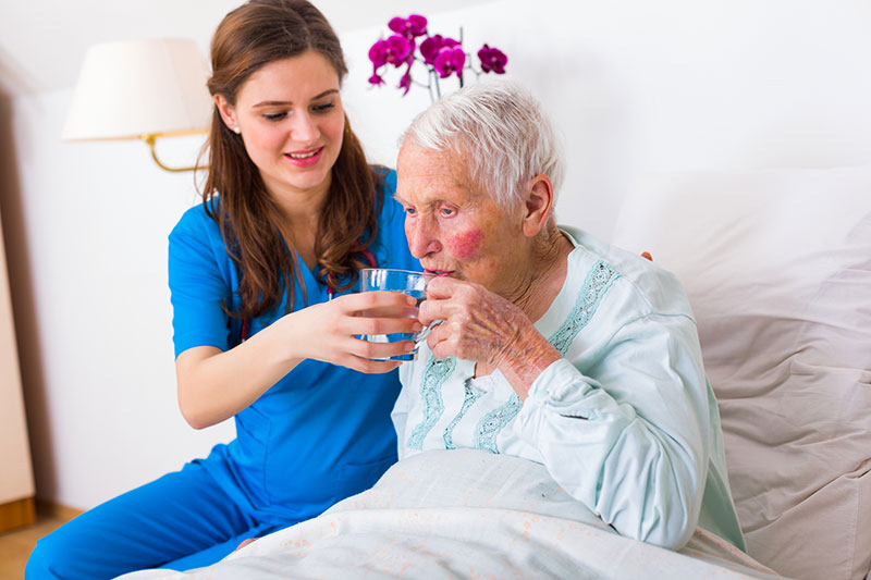 Kind geriatric doctor bringing water to the senior woman in need.