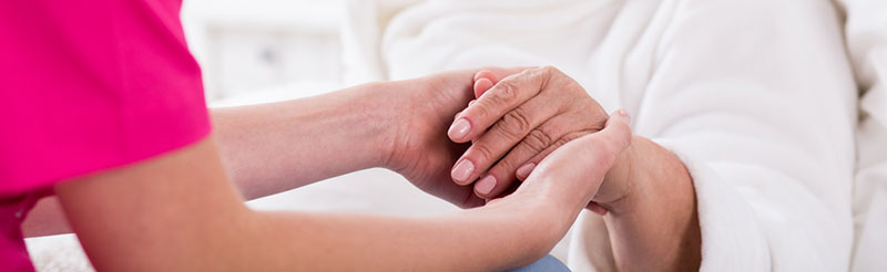 Nurse holding older woman's hand in nursisng home